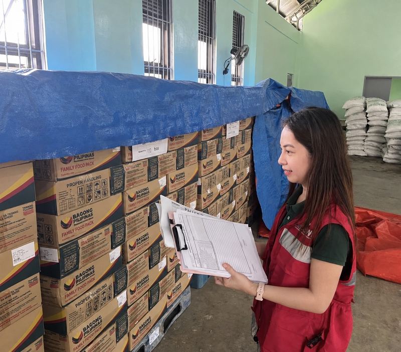 Mary Joice checking a stack of family food packs against her inspection checklist in a warehouse